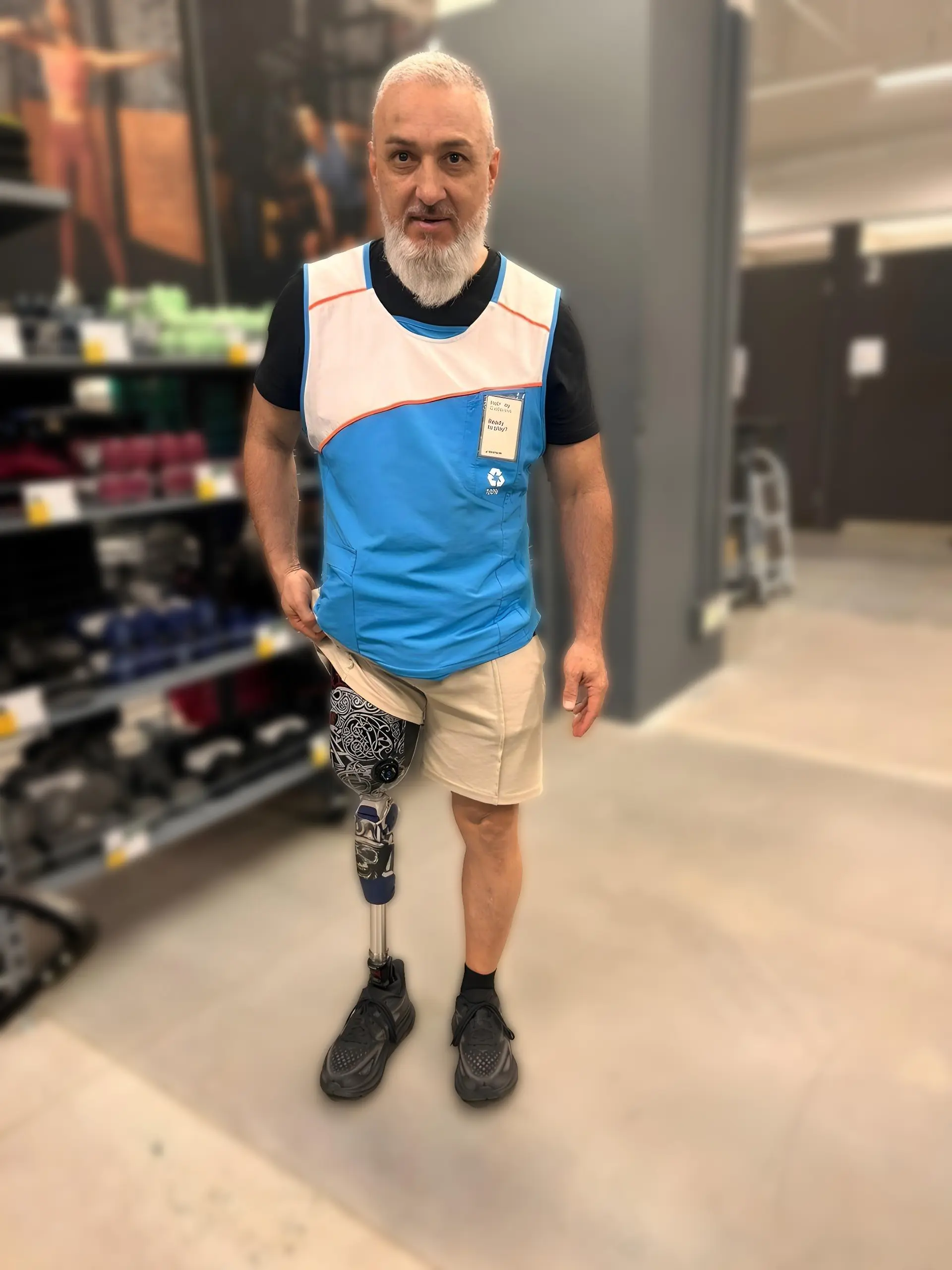 Hombre con prótesis de pierna personalizada en una tienda deportiva, vistiendo uniforme de trabajo y mostrando autonomía y seguridad.